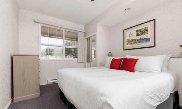 Een hotelkamer met een bed, een raam, een deur en een aan de muur hangend schilderij.
