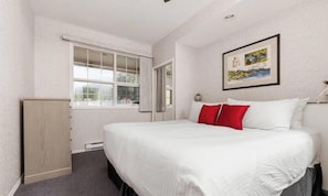 A hotel room with a bed, a window, a door, and a wall-mounted picture.