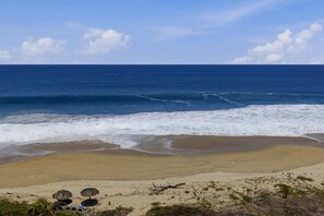Ein Strand mit Wellen, blauem Himmel und einigen Sonnenschirmen.
