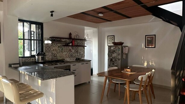 A modern kitchen with a central island, a dining area with a wooden table and chairs, and a staircase leading to an upper level. - Country House in Quindío Casa Victoria (Calarcá)