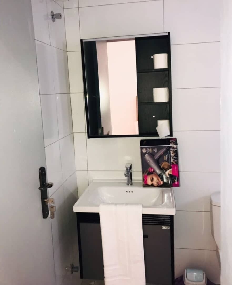 Un baño con lavamanos blanco, un espejo y un perchero para toallas.