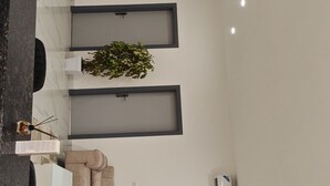 Ein modernes Wohnzimmer mit Flachbildfernseher, einem beigefarbenen Sofa, einem Esstisch und einer Zimmerpflanze.