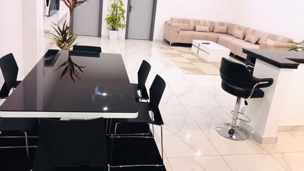 Ein modernes Wohnzimmer mit einer Couch, einem Esstisch mit Stühlen, einer Küchenzeile und einer Bar mit einem Hocker.