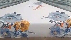 Ein Bett mit Blumenmuster auf der Tagesdecke, zwei Kissen und einem Kopfteil.