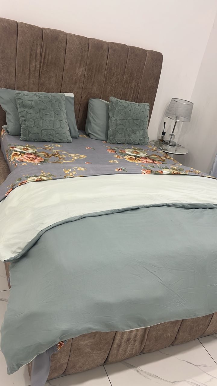 Una cama con una colcha estampada con motivos florales, almohadas verdes y un cabecero de madera.