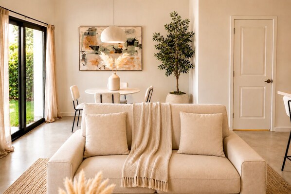 Un salon avec un canapé, une table, des chaises, une plante en pot, un tableau et une porte.