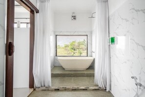 Une salle de bain avec une baignoire sur pieds, une douche et une fenêtre avec des stores.