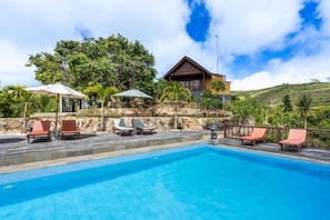 Ein Schwimmbad mit Liegestühlen, einer Steinmauer und einem Holzhaus mit Balkon.