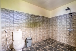 A bathroom with a toilet, a trash bin, and a shower. - Cozzy Pini Sentana Village Nusa Penida  (Klungkung)