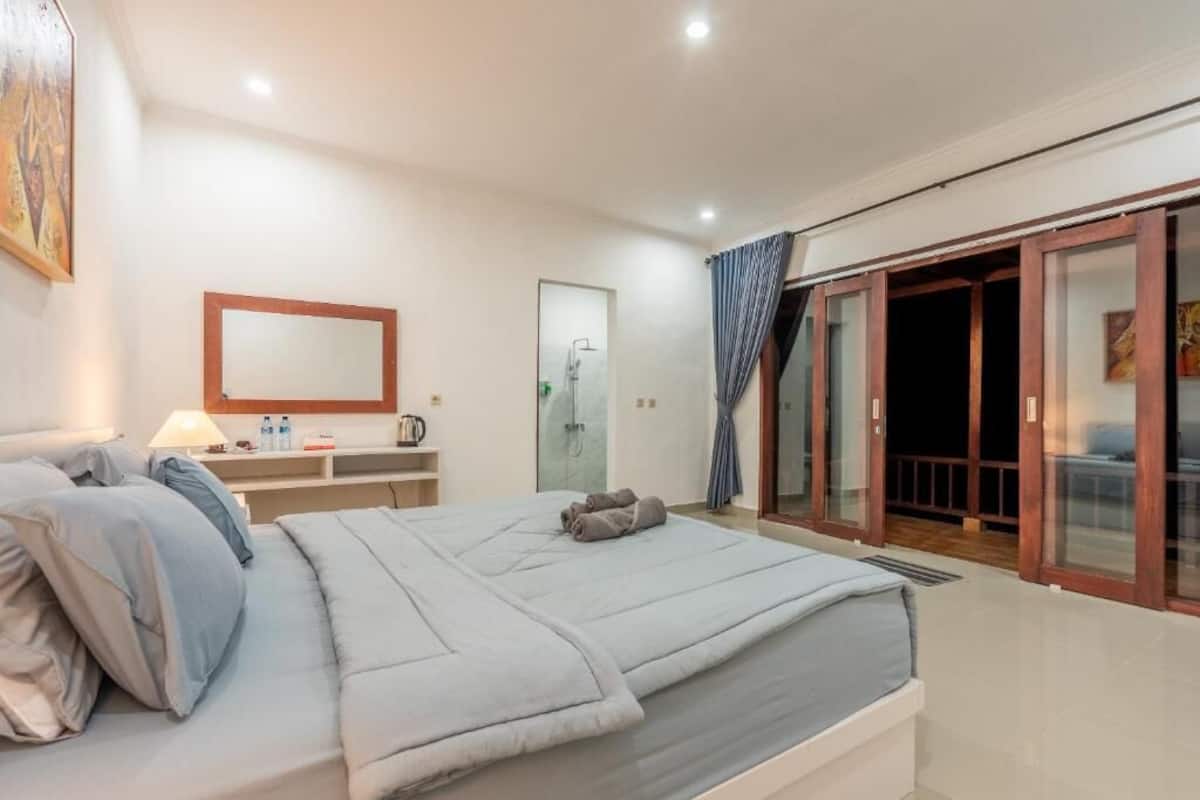 Quarto com cama, mesa de cabeceira, abajur e vista para área externa através de uma porta de vidro.