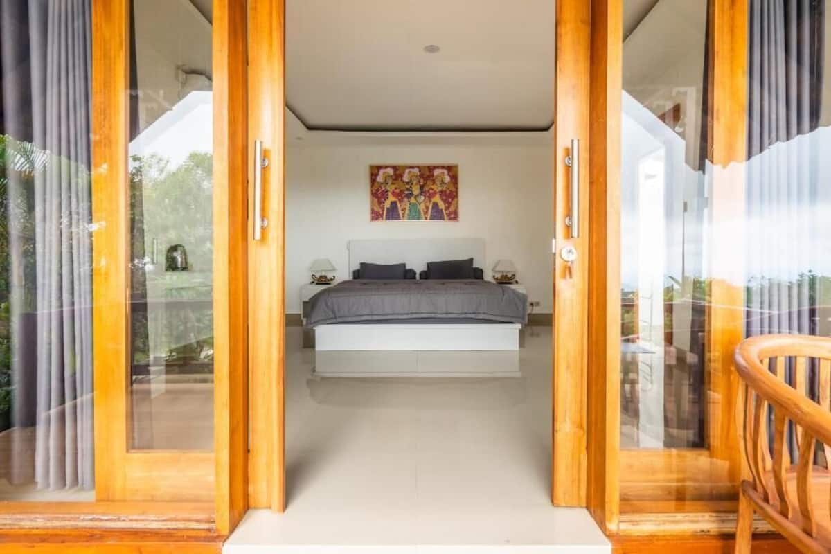 Quarto com uma cama, um quadro na parede e vista através de portas de vidro.