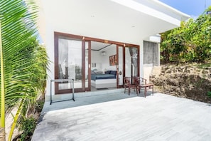 A modern house with a large sliding glass door leading to a bedroom with a bed, a chair, and a table. - Cozzy Pini Sentana Village Nusa Penida  (Klungkung)
