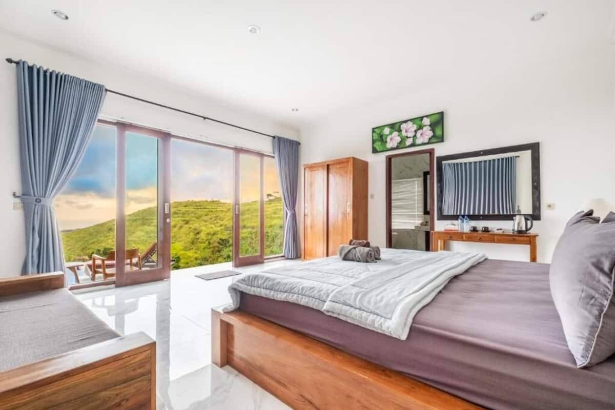 Quarto com uma cama grande, um guarda-roupa de madeira, um espelho e vista para uma paisagem verde.
