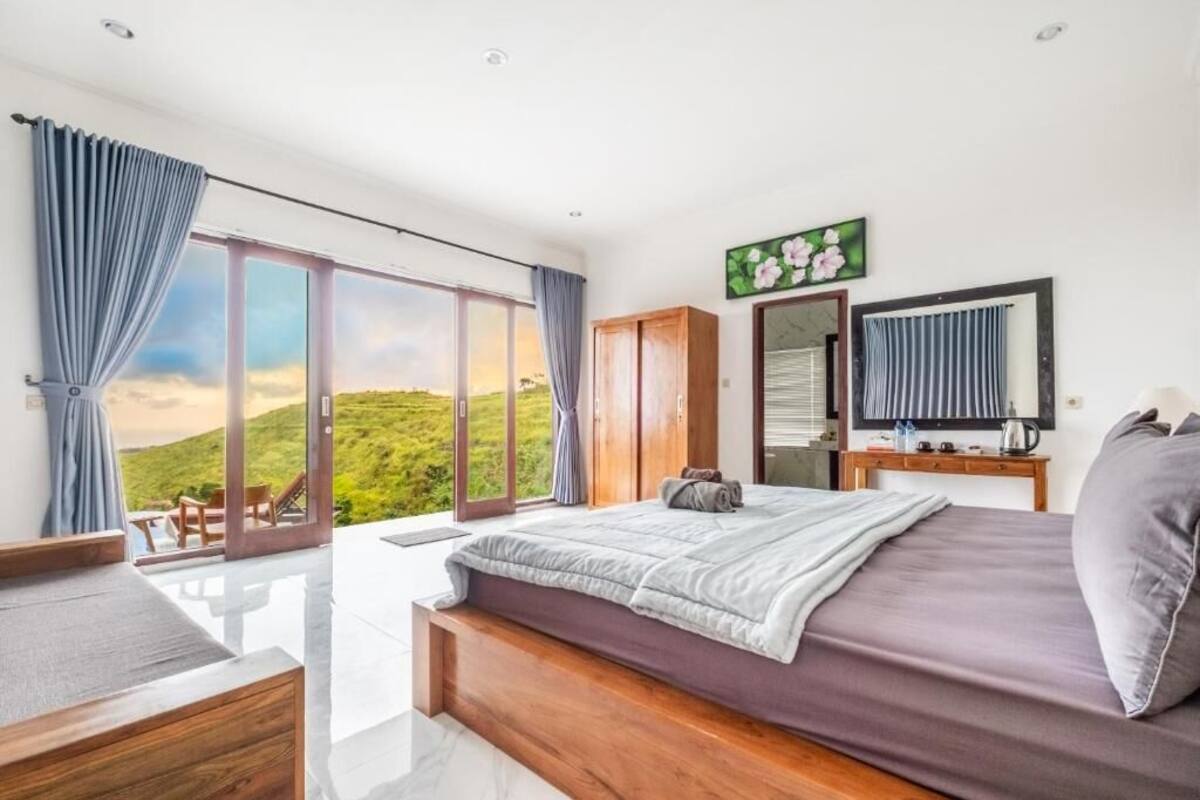 Ein Schlafzimmer mit einem großen Bett, einem Holzschrank, einem Spiegel und Blick auf eine grüne Landschaft.