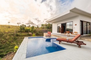 Ein modernes Haus mit Swimmingpool, Sitzgelegenheit im Freien und Blick auf die Landschaft.