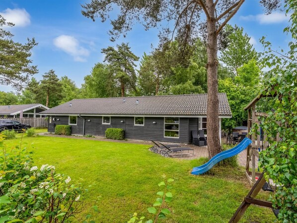 A residential building with a tiled roof, a grassy yard, a blue slide, and a wooden deck. - "Sissa" - 700m from the sea by Interhome (Væggerløse)