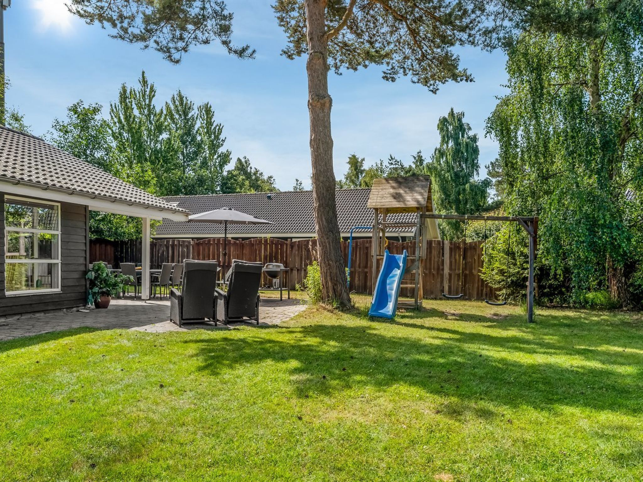 Un jardin avec une terrasse, du mobilier d’extérieur, un toboggan et une cabane en bois.