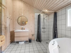 Een badkamer met een houten wastafel, een ronde spiegel, een douche met gordijn en een bad.