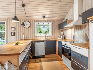 Eine moderne Küche mit Holzschnitzereien, einem eingebauten Geschirrspüler, einem Herd und Pendelleuchten.