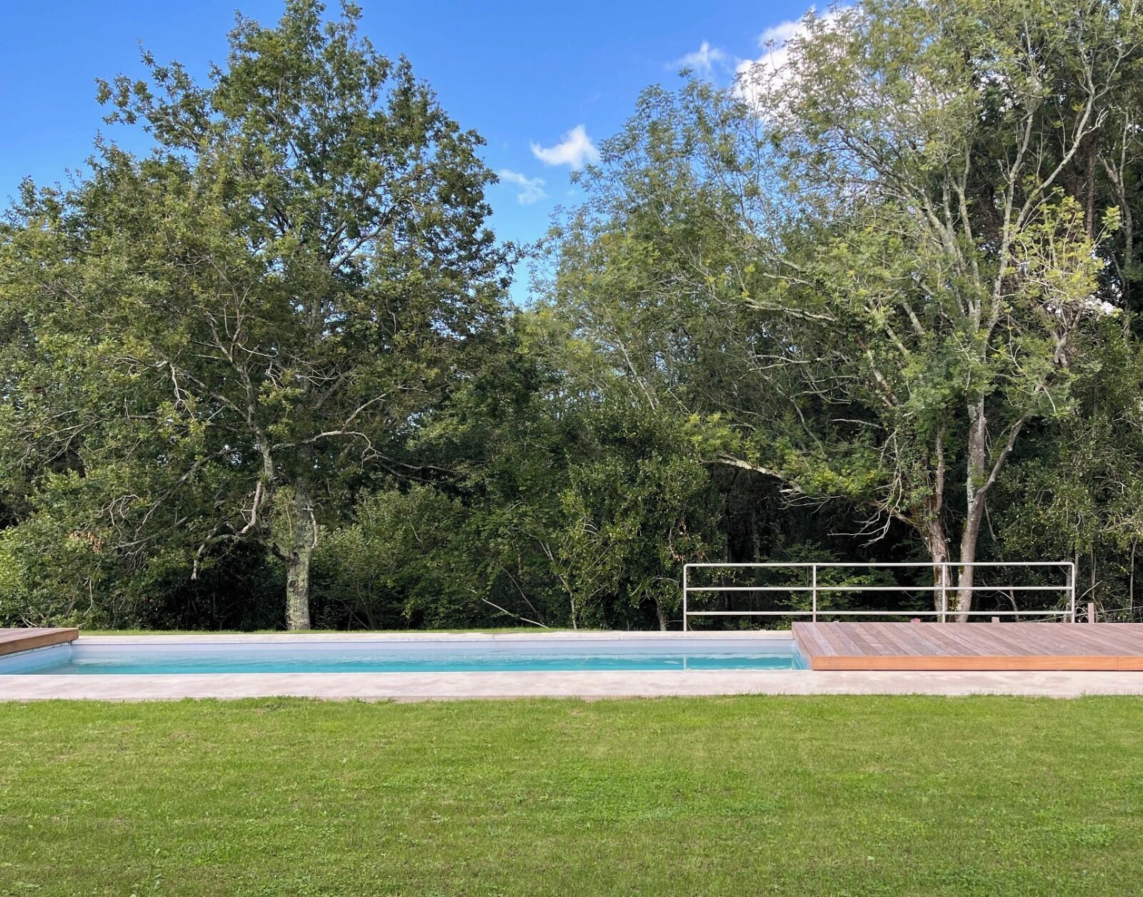 A swimming pool with a wooden deck, surrounded by a grassy lawn and trees.