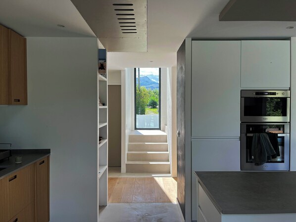 A modern kitchen with built-in appliances, a staircase leading to a balcony, and a view of greenery. - Modern house between sea and mountains - Basque Country - Saint-Jean-de-Luz / Ascain (Ascain)