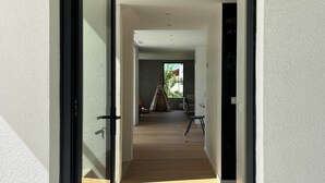 Un corridoio con una porta scorrevole in vetro, un pavimento in legno e una porta nera sulla destra.