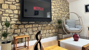 Un soggiorno con parete in pietra, televisore a parete, tavolo in legno, sedia in vimini e piante in vaso.