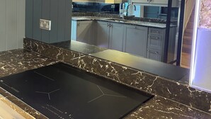 Una cucina moderna con piano cottura a induzione nero, mobili grigi e un'isola in marmo.