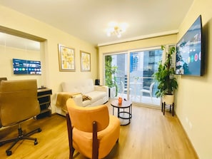 A modern living room with a sofa, armchair, TV, and a balcony with plants. - Executive Apart San Isidro Pool Gym AC (San Isidro)