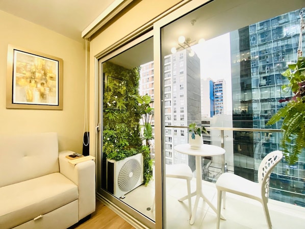 Ein Balkon mit Glastür, einem weißen Stuhl, einem kleinen Tisch und einem Blumentopf.