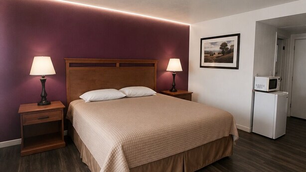 A hotel room with a bed, two bedside tables with lamps, a small refrigerator, and a framed picture on the wall. - Budget Inn Ontario (Ontario)