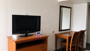 A hotel room with a wooden dresser, a television, a desk with a chair, and a bed with a blanket. - Budget Inn Ontario (Ontario)