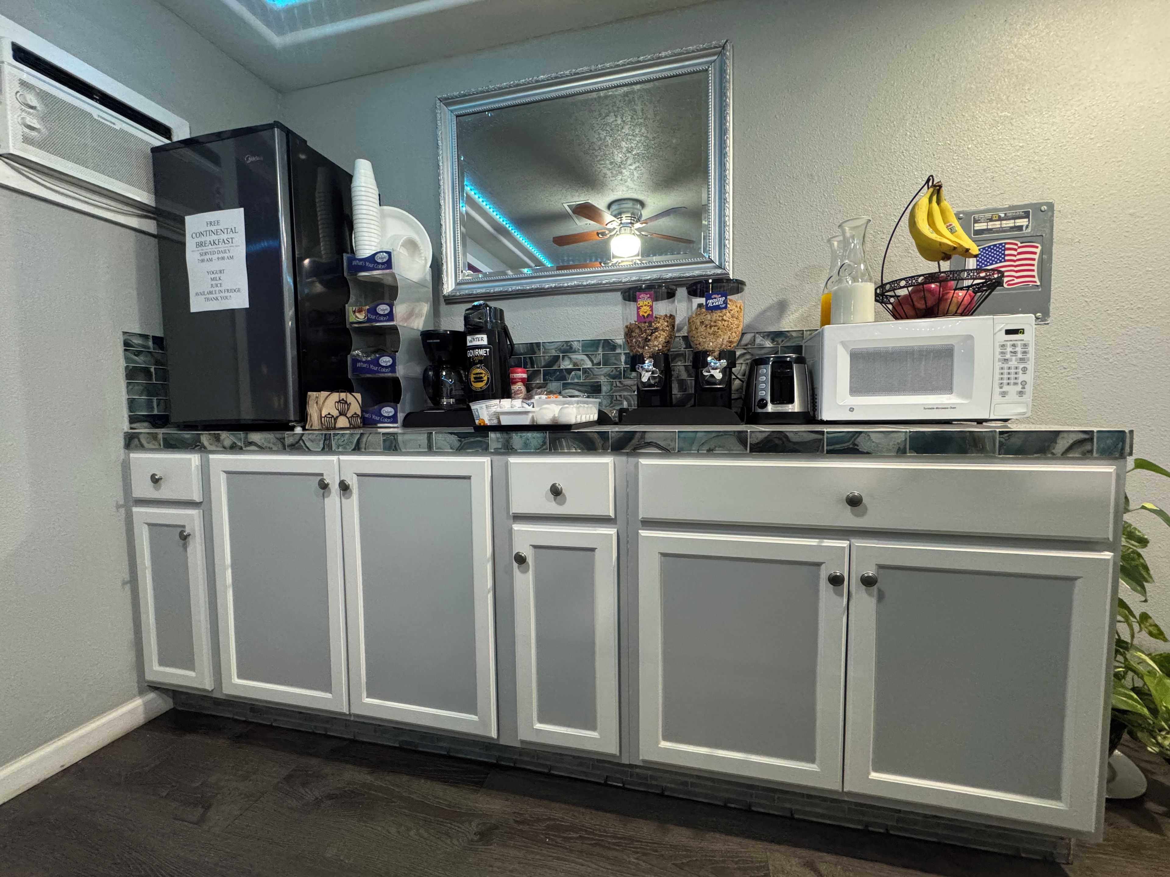 Una kitchenette equipada con refrigerador, microondas, cafetera y diversos alimentos.