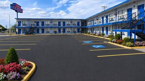 A motel with a blue and white exterior, a parking lot, and a clear sky. - Budget Inn Ontario (Ontario)