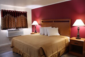 A hotel room with a large bed, two bedside tables with lamps, a window with curtains, and an air conditioning unit. - Budget Inn Ontario (Ontario)