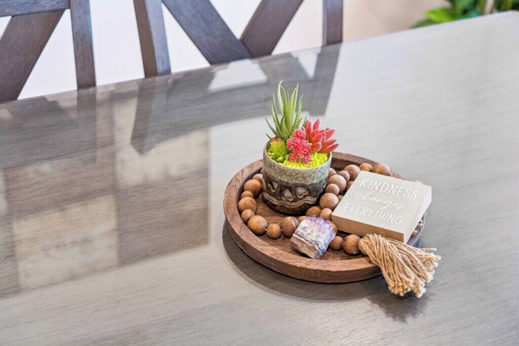 A wooden table with a decorative centerpiece including a small potted plant, a candle, and a card.