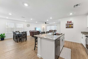 Eine moderne Küche mit Kochinsel, Essbereich mit Stühlen und Wohnbereich mit einer Couch.