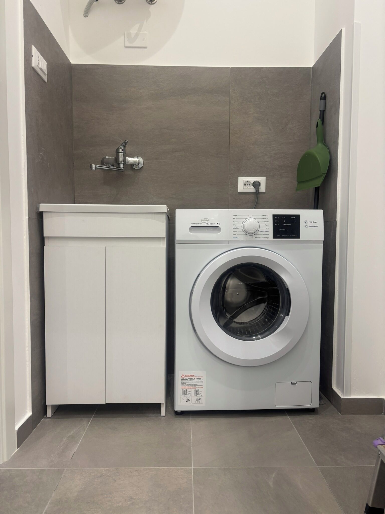 A compact laundry room with a washing machine, a sink, and a green shovel.
