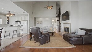 A spacious living area with a fireplace, leather seating, a kitchen with white cabinets, and a ceiling fan. - Spacious Waterfront House w/ boat ramp - sleeps 12 (Bay St. Louis)