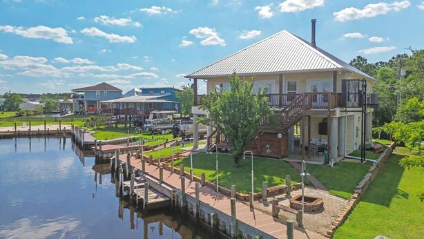 A waterfront property with a dock, a covered patio, and a large house with a balcony. - Spacious Waterfront House w/ boat ramp - sleeps 12 (Bay St. Louis)