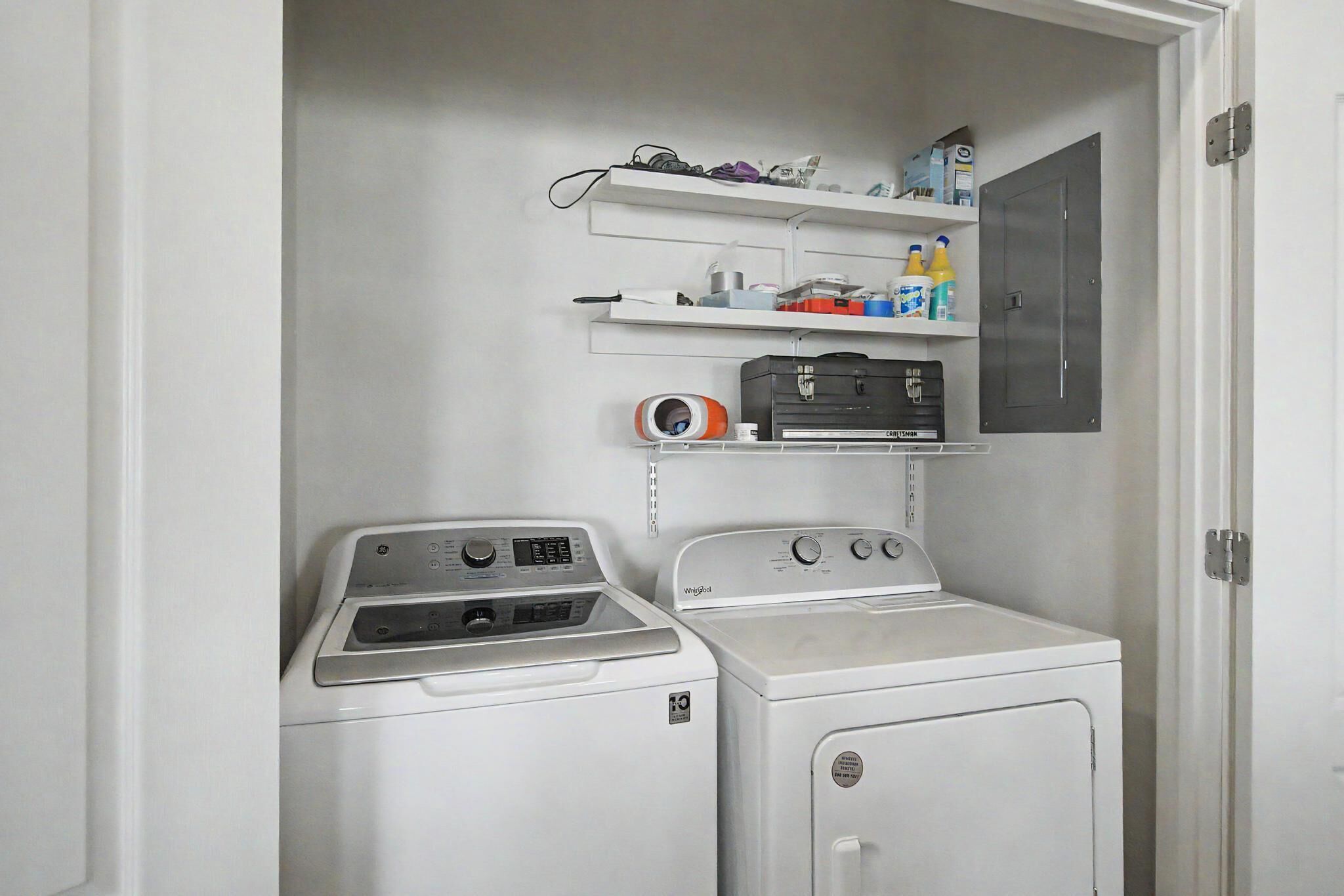 Ett tvättrum med två tvättmaskiner, en torktumlare och hyllor med diverse föremål.