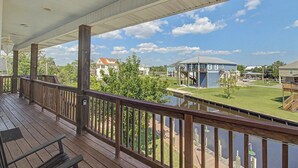 A covered outdoor area with wooden railings, a bench, and a view of a grassy area with a building and a water body. - Spacious Waterfront House w/ boat ramp - sleeps 12 (Bay St. Louis)