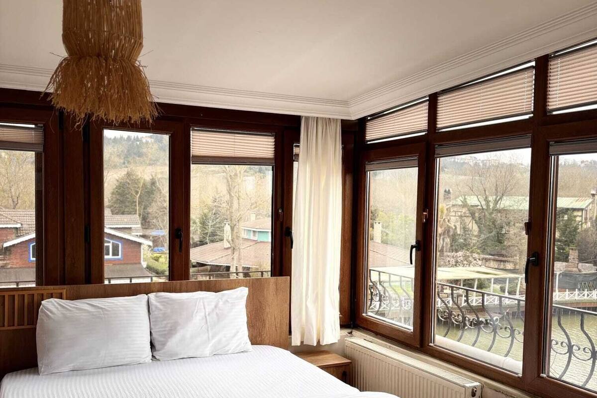 A bedroom with a large bed, wooden headboard, and multiple windows with blinds.