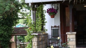 Una casa con un porche de piedra, una silla y una maceta colgante.