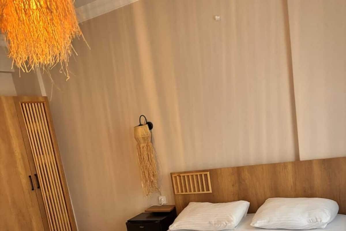 A bedroom with a wooden bed, a nightstand, a wardrobe, and a hanging light fixture.
