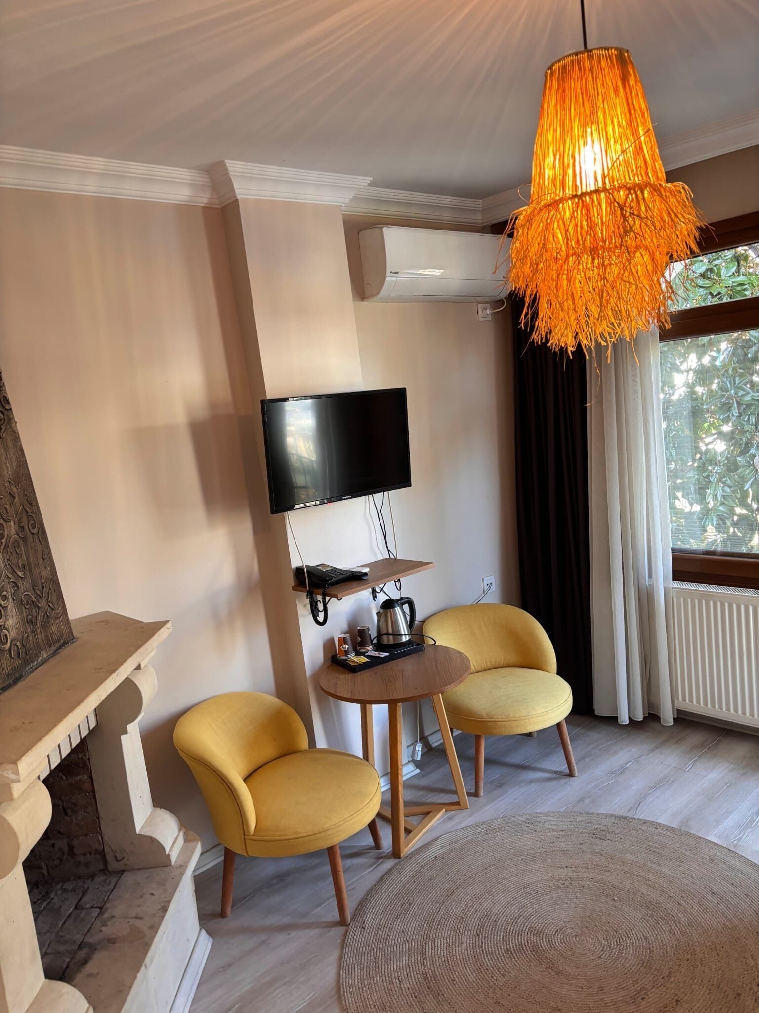 A modern living room with a round coffee table, two yellow armchairs, a mounted flat-screen TV, and a unique orange hanging light fixture.