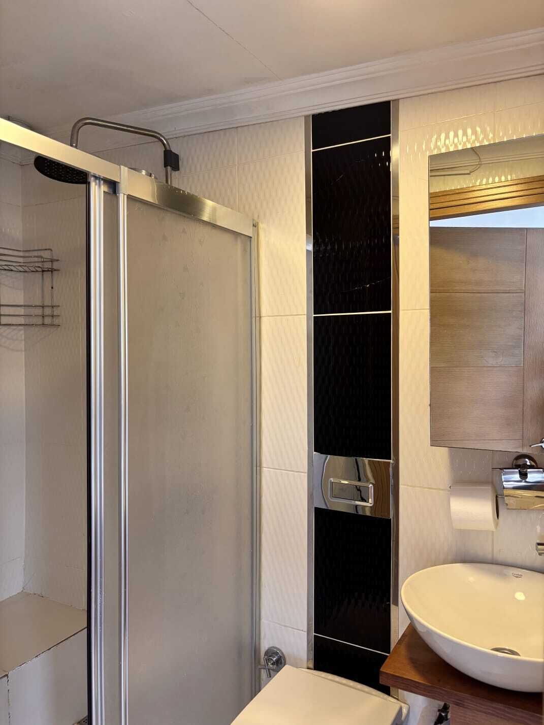 A modern bathroom with a glass shower enclosure, a white sink, and a wooden vanity.