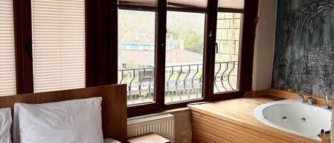 Habitación de hotel con una cama grande, una bañera de madera y vistas al exterior.