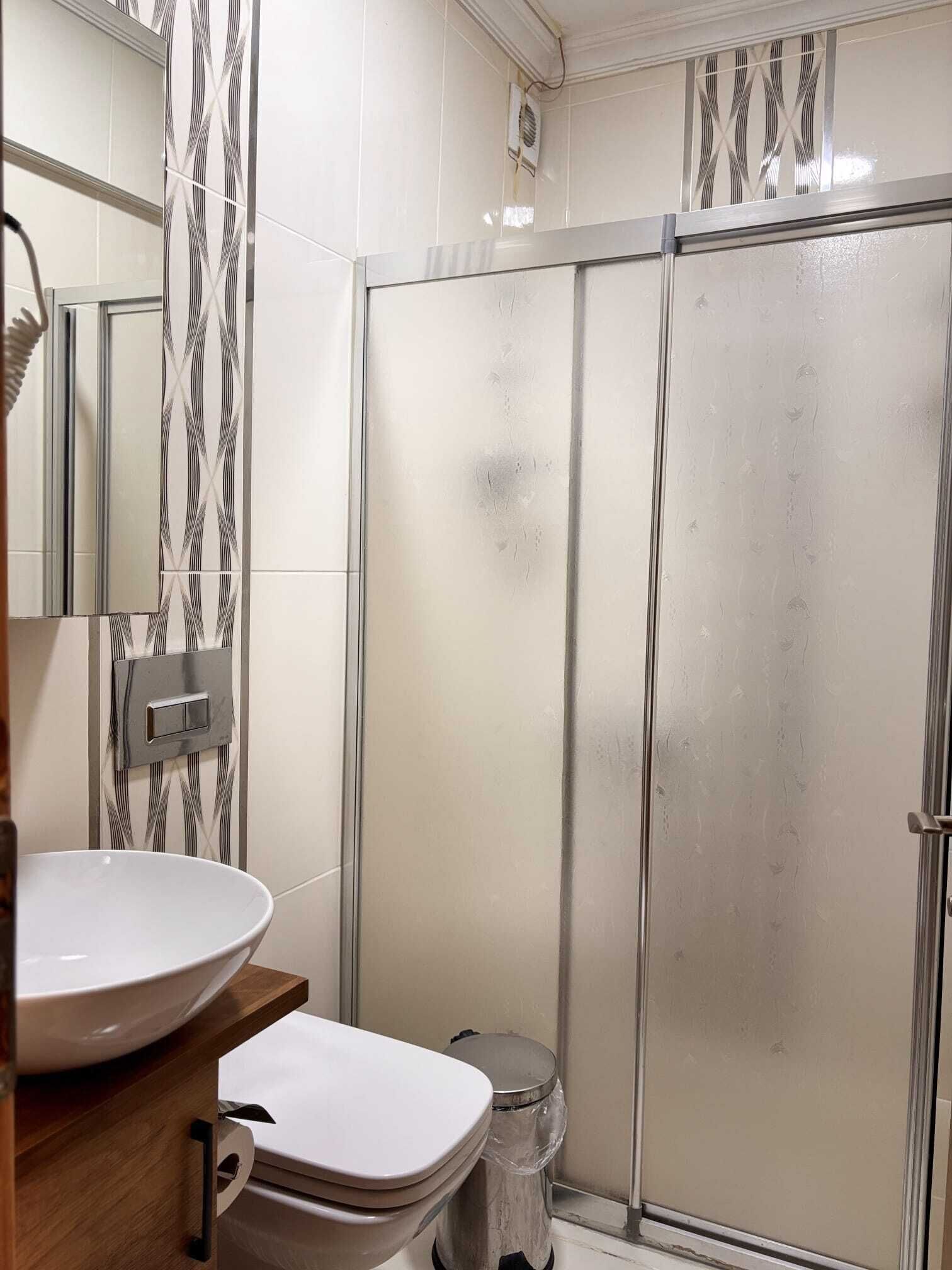 A bathroom with a white sink, toilet, and a glass-enclosed shower area.