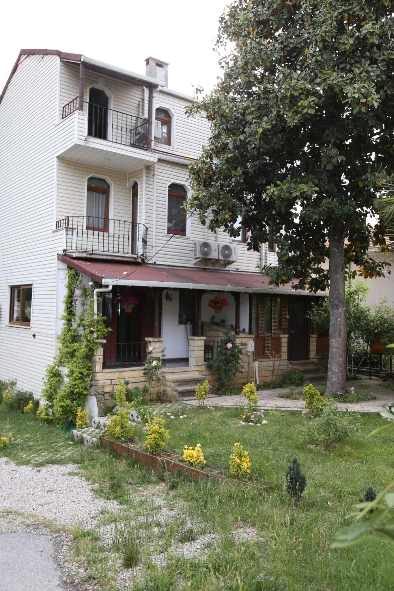 A two-story house with a front porch, a small garden, and a tree.